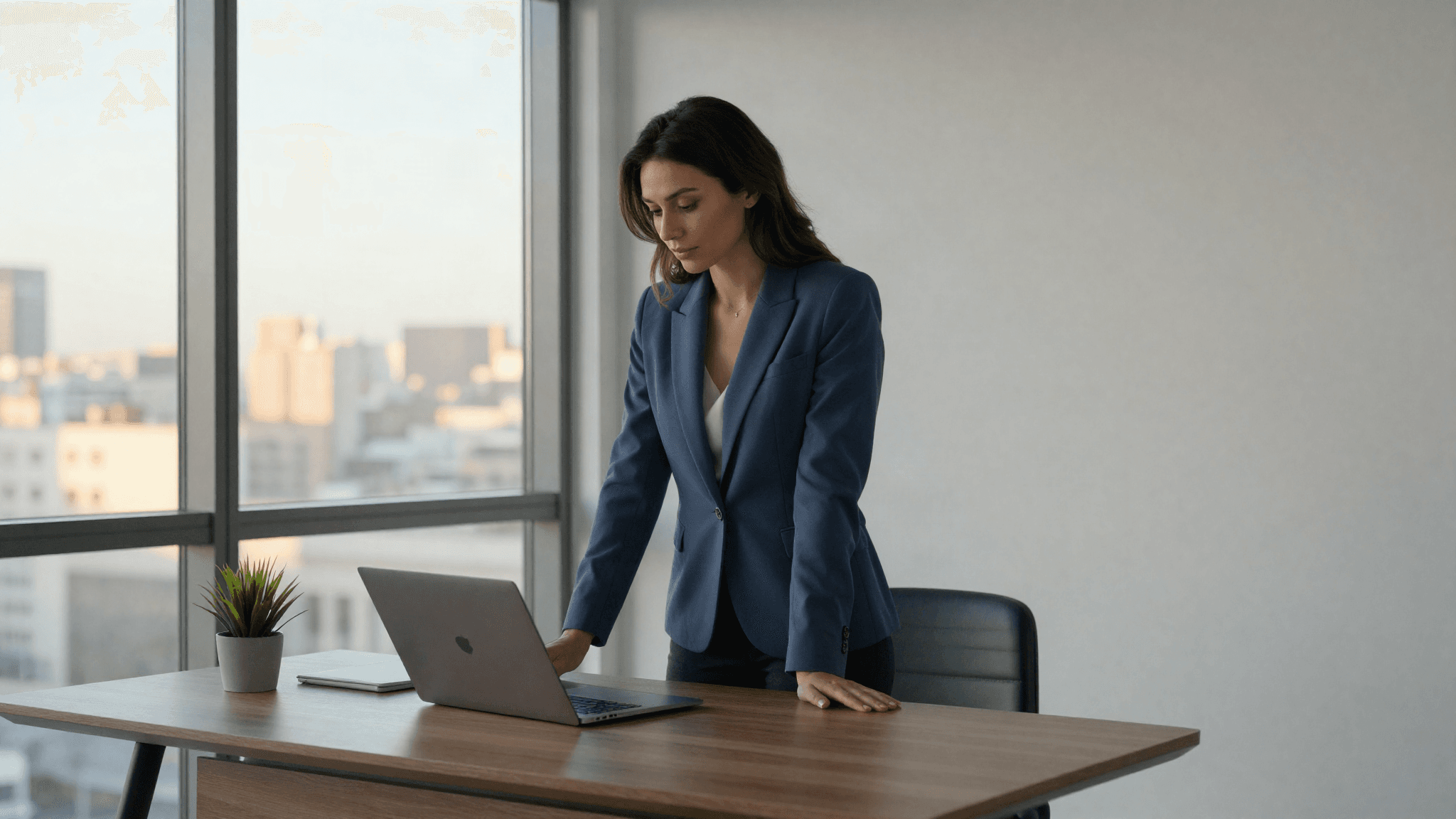 An executive in a modern corner office reviewing a laptop